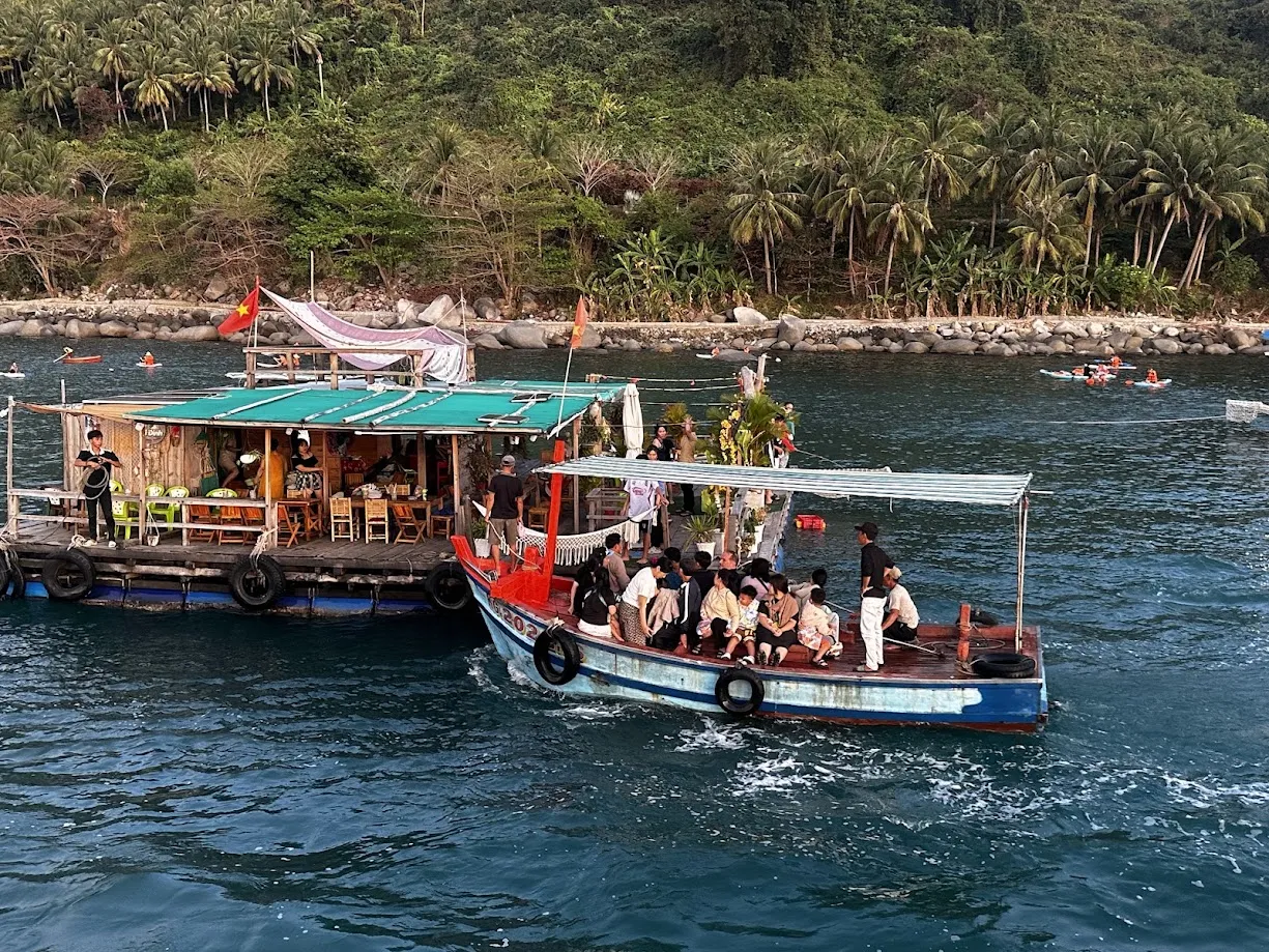 Ghe gỗ chở khách cập vào nhà bè tại Hòn Sơn, phía xa có khách chèo SUP