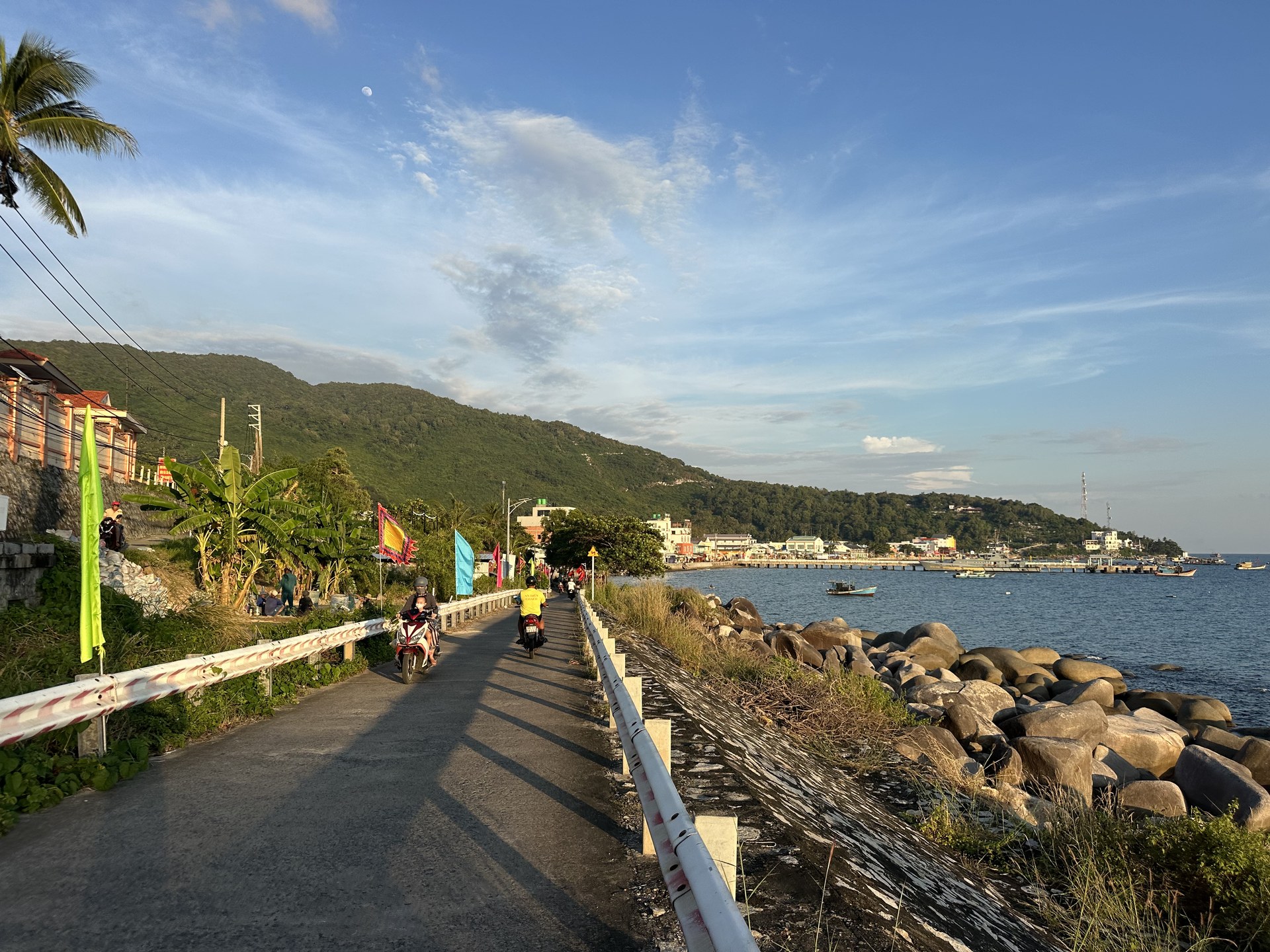 The coast road into the village in the late afternoon, with motorbikes and the pier in the distance