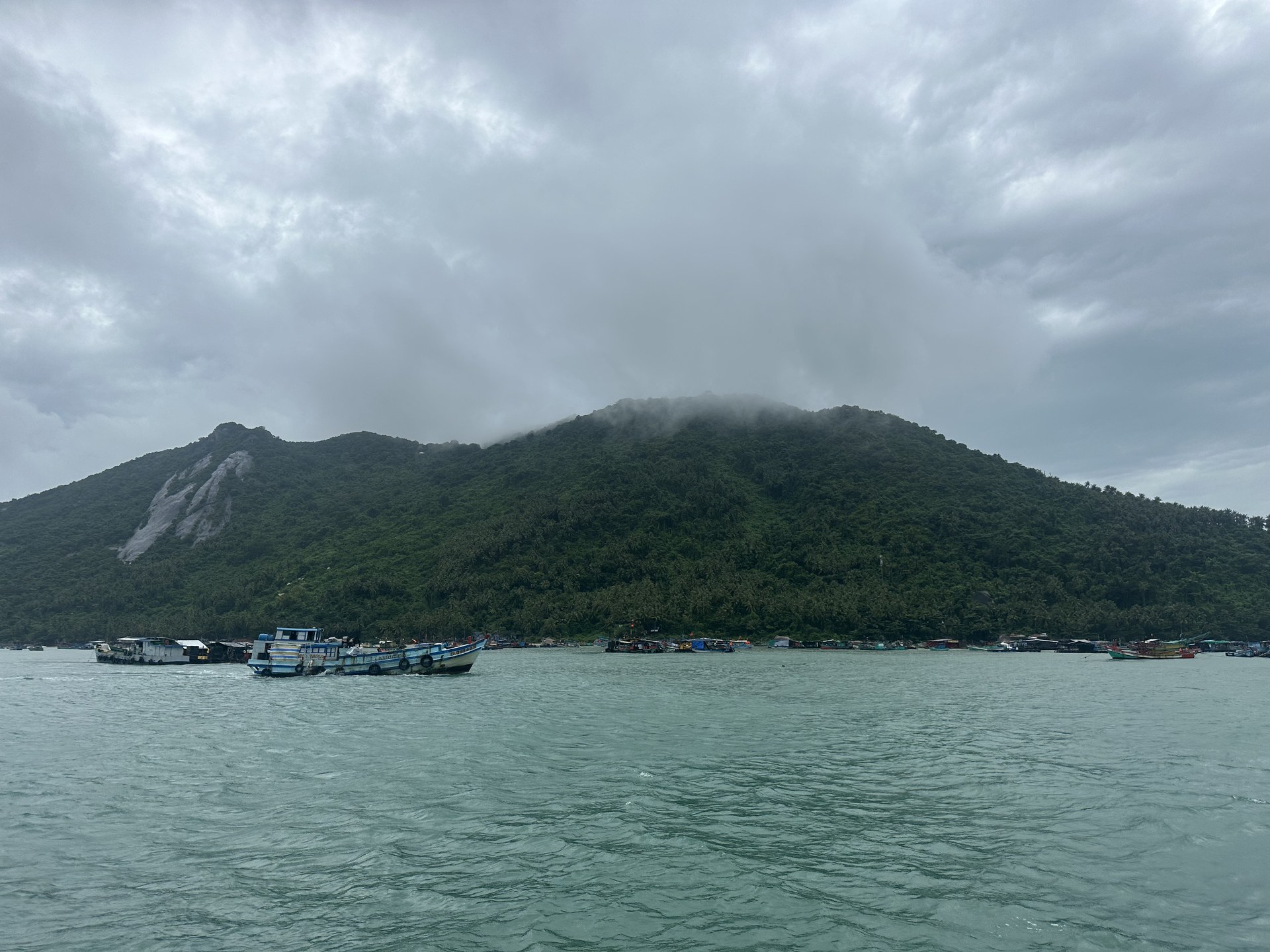 Raft houses and fishing boats moored close under the mountain on a cloudy day